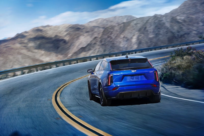 Rear View of a Blue 2026 OPTIQ-V Driving on a Curve of a Mountain Row | Cadillac of Rexburg in Rexburg ID
