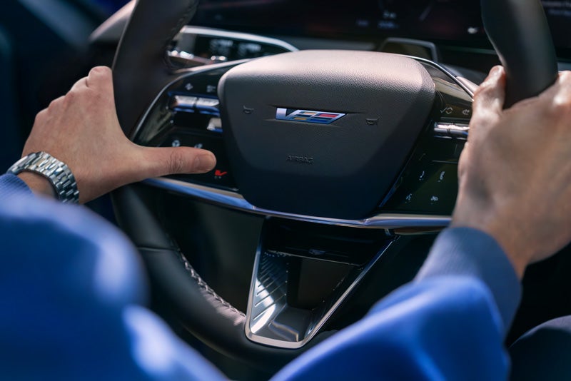 Close-up of a Man About to Press the V-Button on the 2026 OPTIQ-V Steering Wheel | Cadillac of Rexburg in Rexburg ID